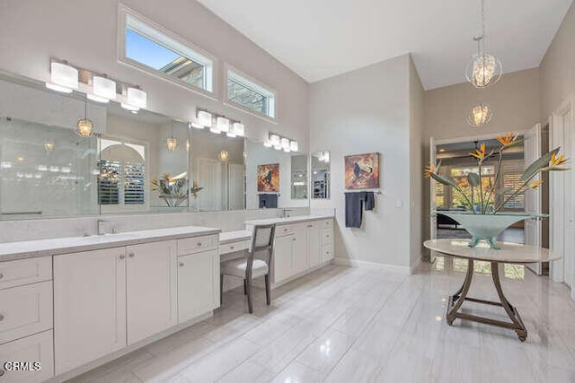 full bathroom with a high ceiling, a chandelier, two vanities, and baseboards