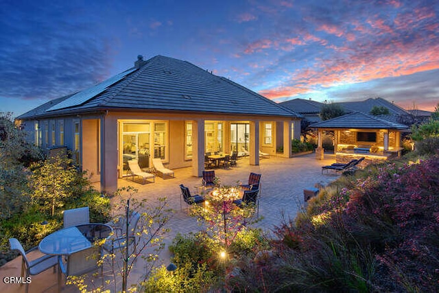 back of house at dusk with a gazebo, outdoor dining area, a fire pit, a patio area, and stucco siding