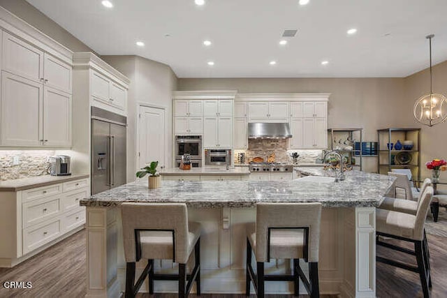kitchen with appliances with stainless steel finishes, under cabinet range hood, decorative backsplash, white cabinets, and a large island