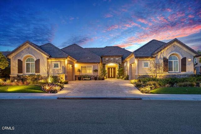 french country style house featuring driveway, stone siding, stucco siding, and an attached garage