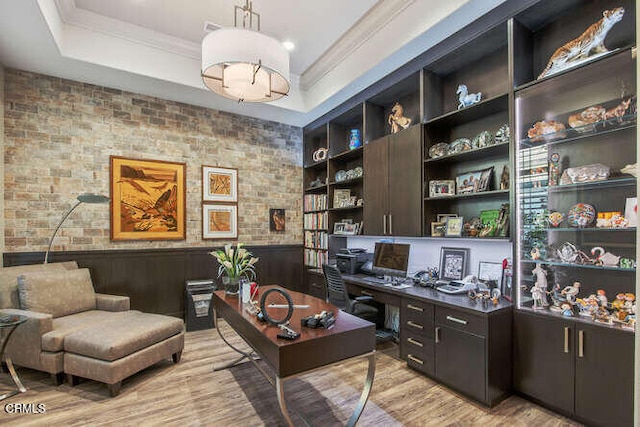 office area with light wood-style flooring, ornamental molding, wainscoting, a raised ceiling, and built in features