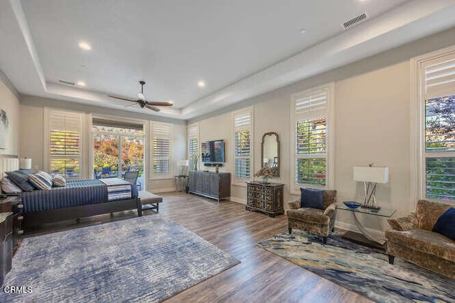 bedroom featuring a raised ceiling, wood finished floors, baseboards, and recessed lighting