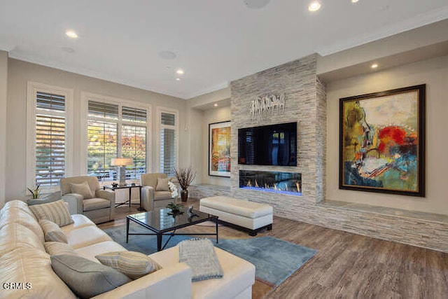 living area featuring recessed lighting, wood finished floors, a stone fireplace, and crown molding