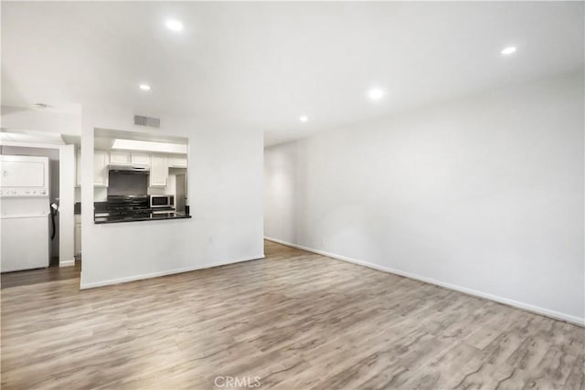 unfurnished living room featuring stacked washing machine and dryer, light wood-style floors, recessed lighting, and baseboards