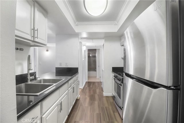 kitchen featuring stainless steel appliances, a sink, dark countertops, white cabinets, and ornamental molding