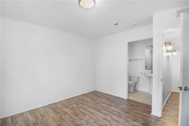unfurnished bedroom featuring wood finished floors and connected bathroom