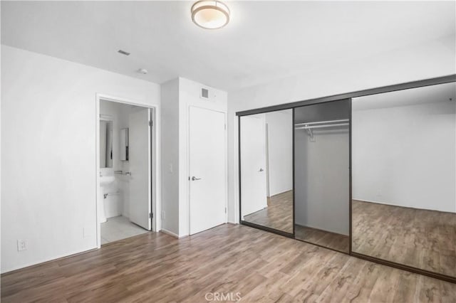 unfurnished bedroom with wood finished floors, a closet, and ensuite bathroom