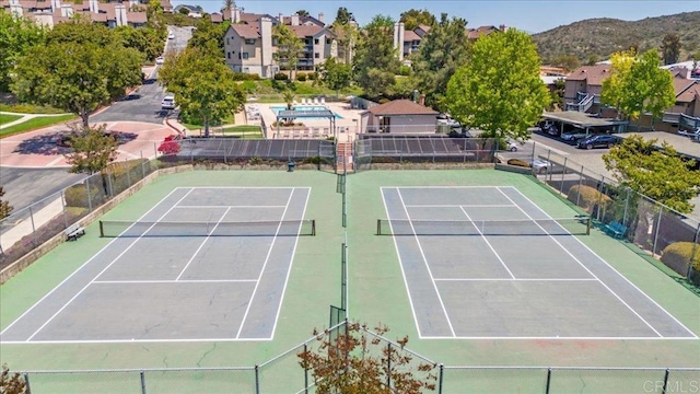 view of tennis court featuring fence, a residential view, and a mountain view