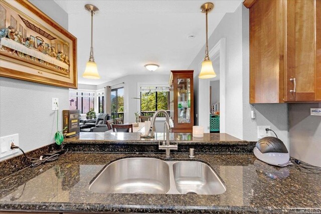 kitchen featuring a sink, a peninsula, brown cabinetry, and dark stone counters