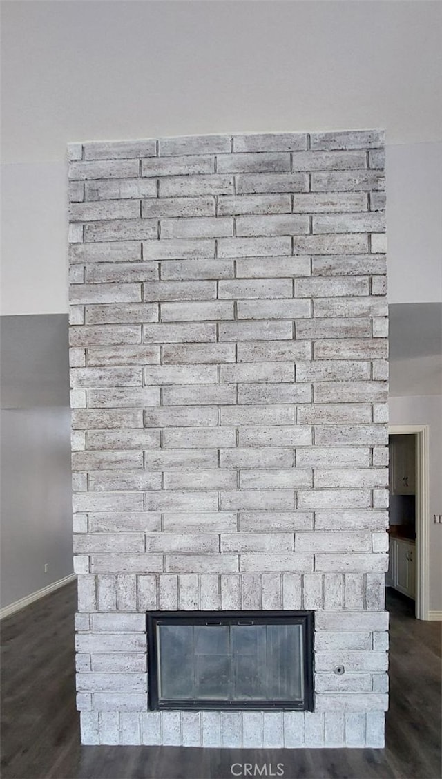 detailed view of a brick fireplace, baseboards, and wood finished floors