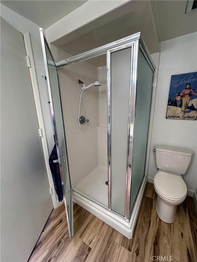 full bathroom featuring wood finished floors, a shower stall, and toilet