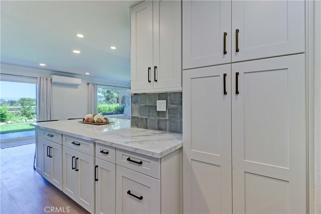 3364 Punta Alta Unit 1E, Laguna Woods, CA 92637 - kitchen featuring a wall unit AC, white cabinets, light stone counters, backsplash, and wood finished floors