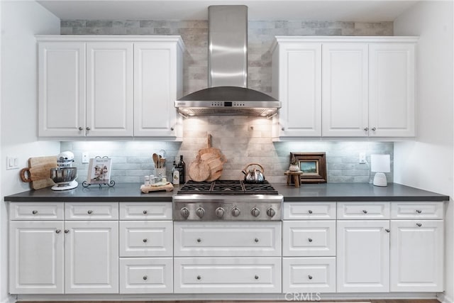 kitchen with wall chimney range hood, stainless steel gas cooktop, dark countertops, and white cabinetry