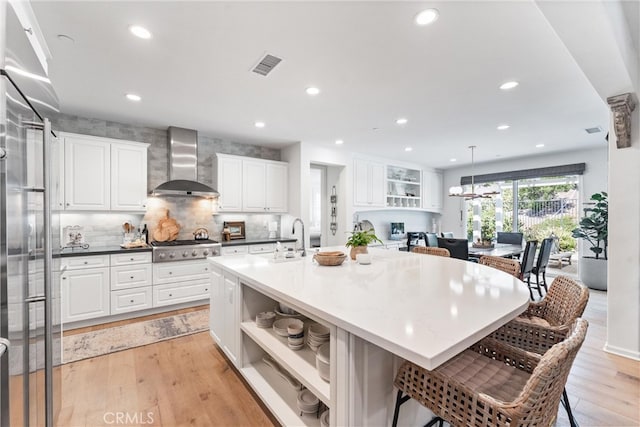 kitchen with wall chimney range hood, open shelves, a sink, white cabinetry, and a breakfast bar area