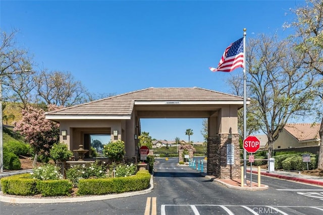 view of asphalt road with traffic signs, curbs, and a gated entry