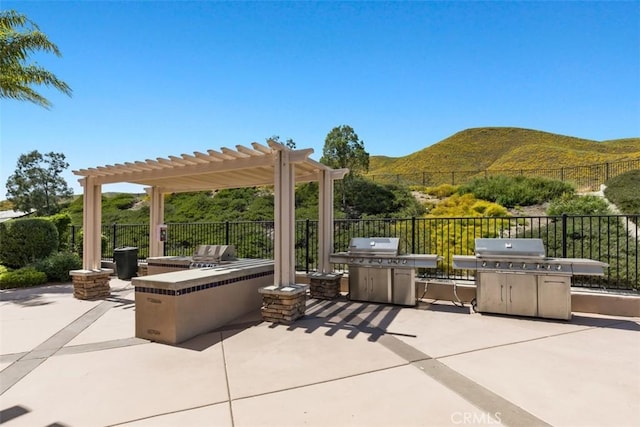 view of patio with an outdoor kitchen, a pergola, a mountain view, fence, and area for grilling