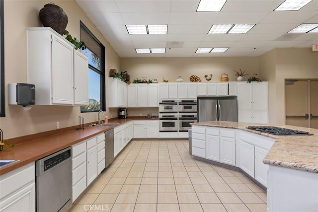 kitchen with appliances with stainless steel finishes, a sink, white cabinets, light tile patterned flooring, and a center island