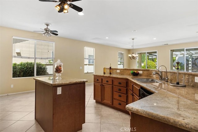 kitchen featuring a sink, a center island, brown cabinetry, light tile patterned flooring, and healthy amount of natural light