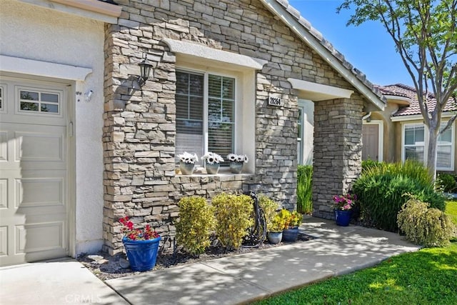 doorway to property with stone siding, stucco siding, and an attached garage