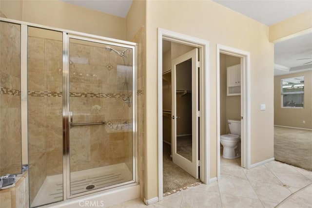 bathroom with a shower stall, toilet, baseboards, and a walk in closet