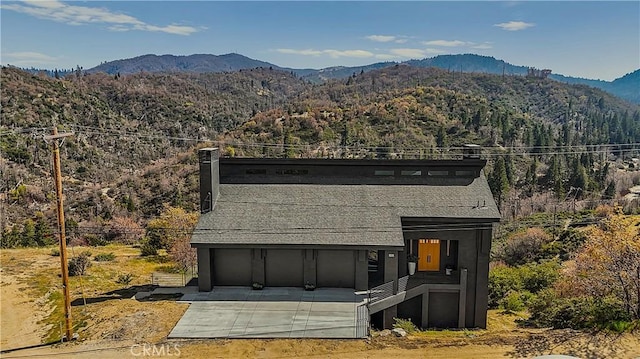 791 Cypress Rd, Lake Arrowhead, CA 92321 - view of front facade featuring a mountain view, a garage, driveway, a chimney, and a view of trees
