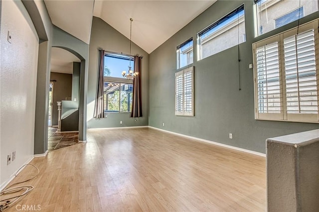 spare room featuring arched walkways, wood finished floors, a chandelier, baseboards, and high vaulted ceiling
