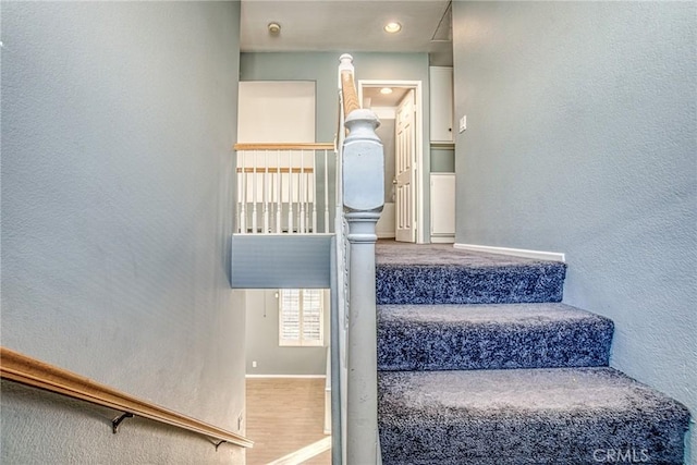 staircase featuring a textured wall, wood finished floors, and baseboards