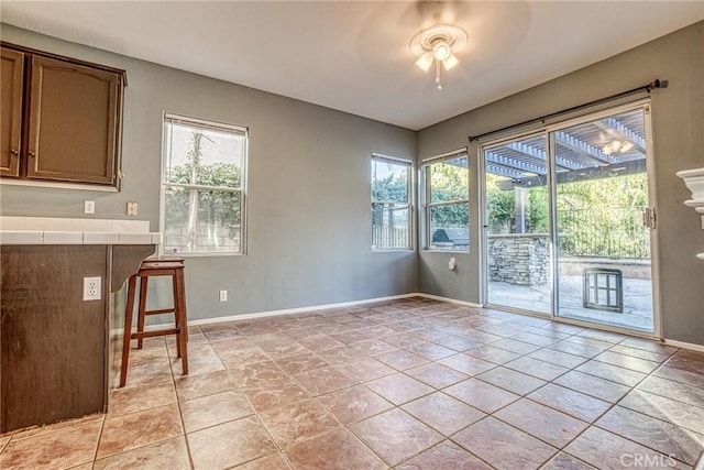 unfurnished dining area with a ceiling fan, baseboards, and light tile patterned flooring