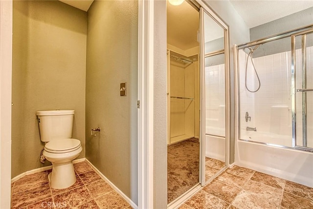 full bath featuring toilet, a textured wall, a spacious closet, and combined bath / shower with glass door