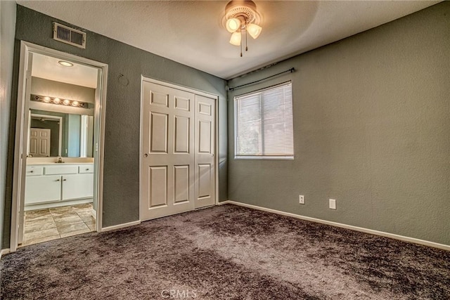 unfurnished bedroom featuring carpet floors, a textured wall, a closet, ensuite bath, and baseboards