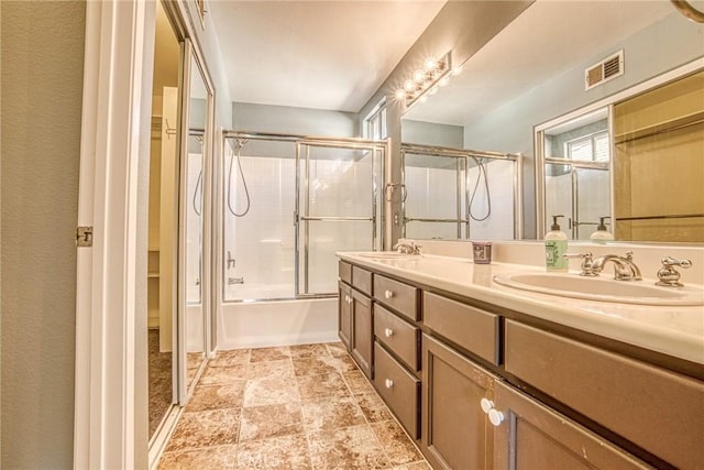 full bathroom with double vanity, stone finish flooring, and shower / bath combination with glass door