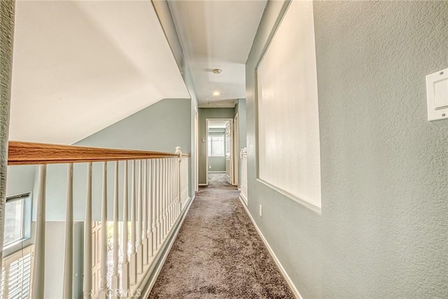 hall with carpet floors, vaulted ceiling, baseboards, and a textured wall