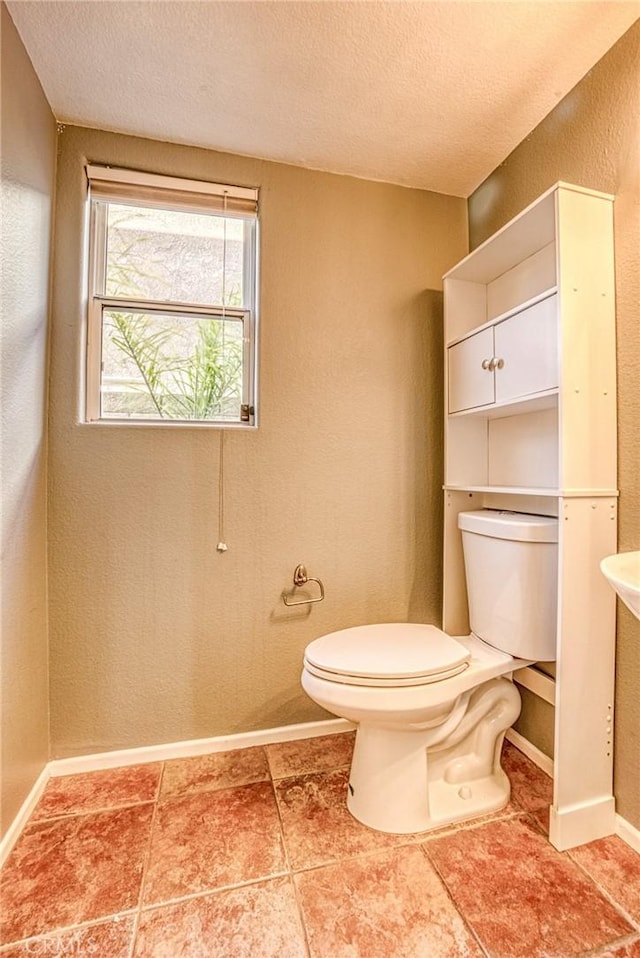 half bath with toilet, a textured ceiling, and baseboards