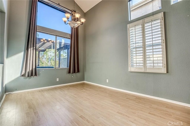 empty room featuring a chandelier, wood finished floors, baseboards, and vaulted ceiling