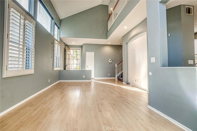 unfurnished room with stairway, wood finished floors, baseboards, and high vaulted ceiling