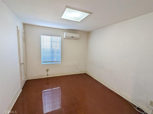 spare room featuring a wall unit AC, dark wood-style flooring, and baseboards