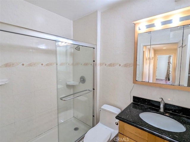 full bath with a stall shower, vanity, toilet, and tile walls