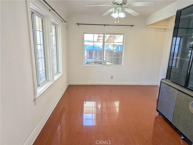 empty room featuring baseboards, wood finished floors, and a ceiling fan