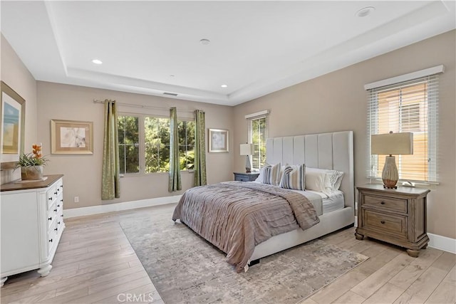 bedroom with baseboards, light wood finished floors, a raised ceiling, and recessed lighting