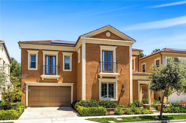 view of front facade with a balcony, roof mounted solar panels, stucco siding, concrete driveway, and a garage