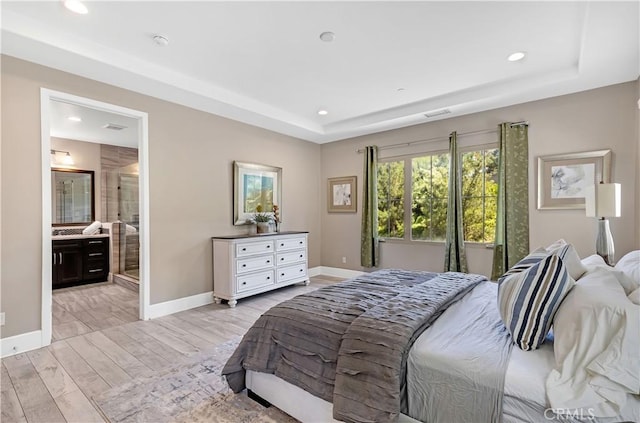 bedroom with a raised ceiling, recessed lighting, baseboards, light wood-type flooring, and ensuite bath