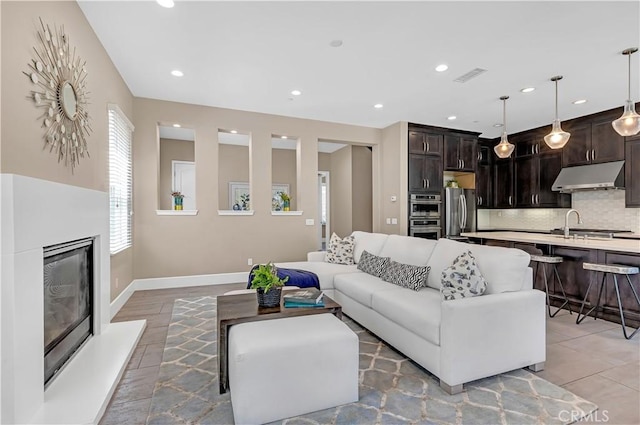 living area featuring a glass covered fireplace, recessed lighting, baseboards, and light tile patterned flooring