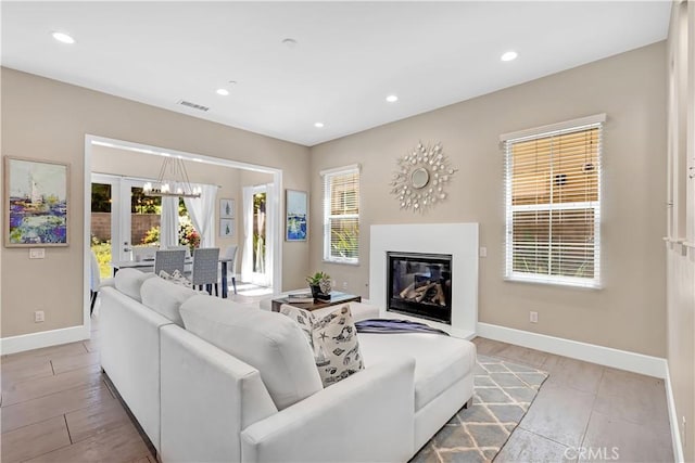living area with a glass covered fireplace, baseboards, plenty of natural light, recessed lighting, and a chandelier