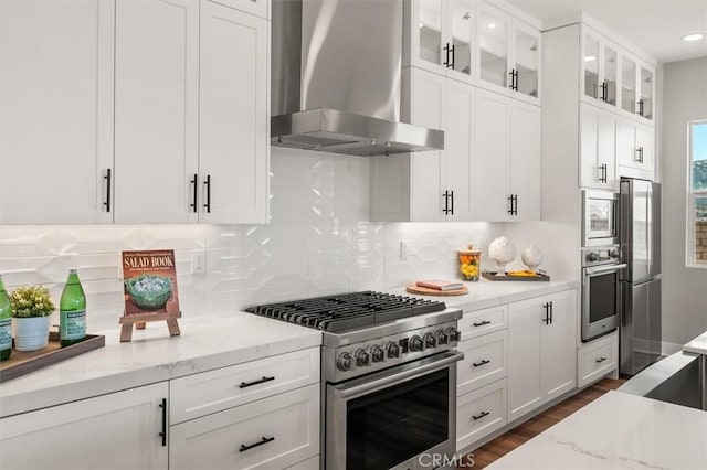 6533 Canyon Oaks Dr, Simi Valley, CA 93063 - kitchen with stainless steel appliances, wall chimney exhaust hood, white cabinetry, light stone counters, and glass insert cabinets
