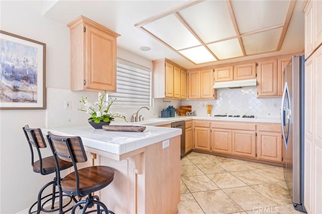 kitchen with light brown cabinets, stainless steel appliances, a sink, a peninsula, and backsplash