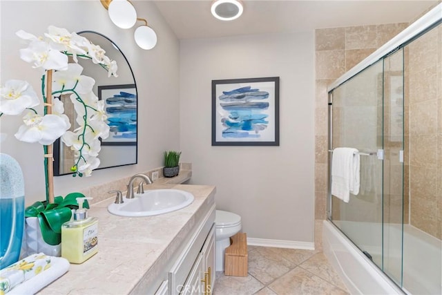 bathroom with vanity, tile patterned floors, toilet, baseboards, and bath / shower combo with glass door