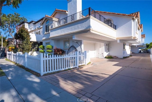 mediterranean / spanish-style home with stucco siding, a fenced front yard, a balcony, driveway, and a tiled roof