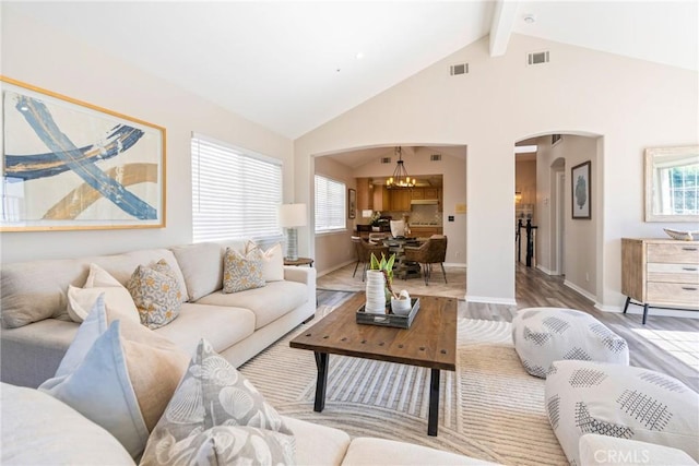 living room with arched walkways, a chandelier, light wood finished floors, beam ceiling, and baseboards