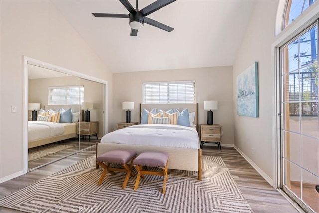 bedroom featuring high vaulted ceiling, wood finished floors, multiple windows, a closet, and baseboards