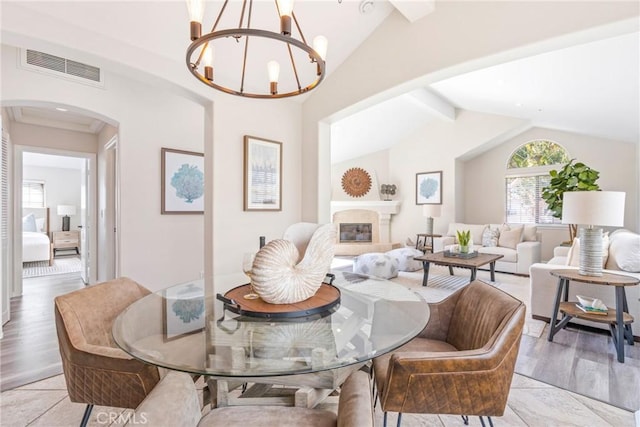 dining area with arched walkways, a chandelier, a glass covered fireplace, and light wood-style flooring